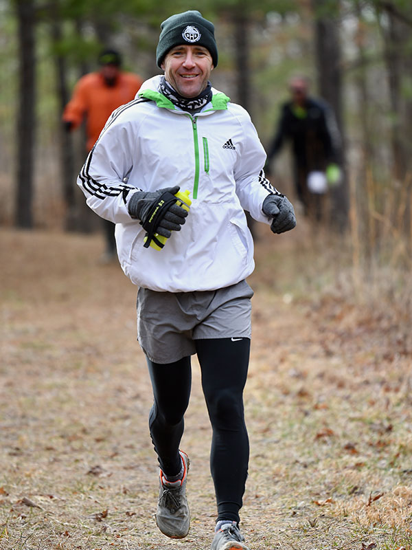 coach josh laker running on a trail on the woods, he is wearing a black stocking hat, white Adidas jacket with lime green stripes 